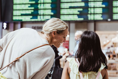 Rear view of smiling mother talking to daughter at railroad station