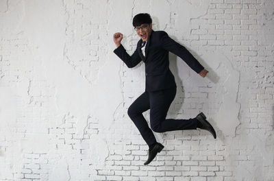 Full length of young man jumping against wall