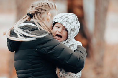 Mother holding crying baby, sad little boy being hugged by his mother