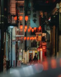 Illuminated street by buildings in city at night