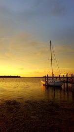 Sailboats moored in sea against sky during sunset