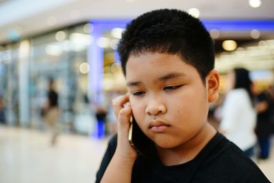Close-up of boy talking on mobile phone in shopping mall