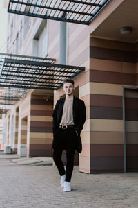 Portrait of young woman standing against building