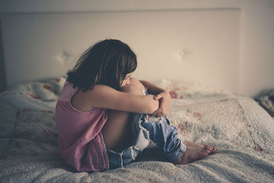 Girl child serious and frustrated sitting on a bed in a bright bedroom, concept age crisis 