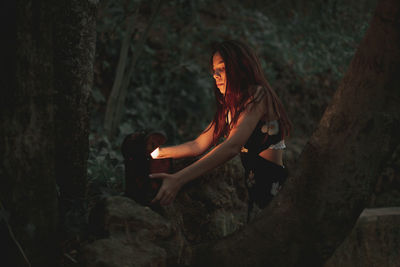 Side view of young woman sitting on tree trunk