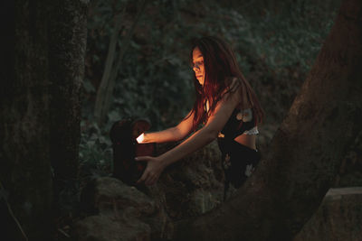 From below of young female in dress taking ancient retro clock in wooden box on stone in autumnal forest