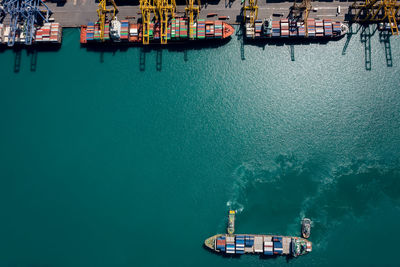 Aerial view container ship and tugboat sailing in sea and commercial port working crane bridge 