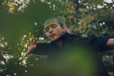 Thoughtful young man dancing with eyes closed against trees 