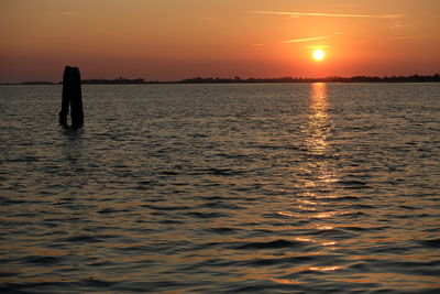 Silhouette man standing in sea against sky during sunset