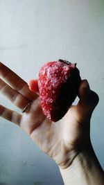 Cropped image of person holding frozen strawberry against wall