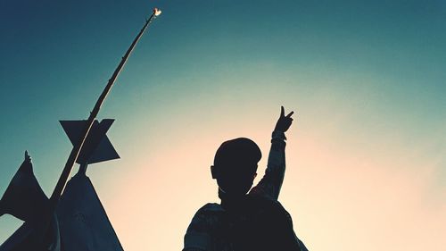 Low angle view of woman showing peace sign against sky at dusk