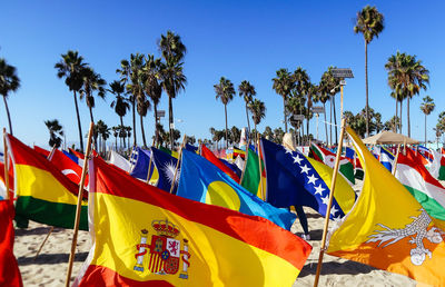 Multi colored flags and palm trees against blue sky