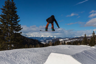 Man jumping on snowcapped mountain against sky