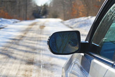 Car side mirror on a dirt road showing a wonan driving.