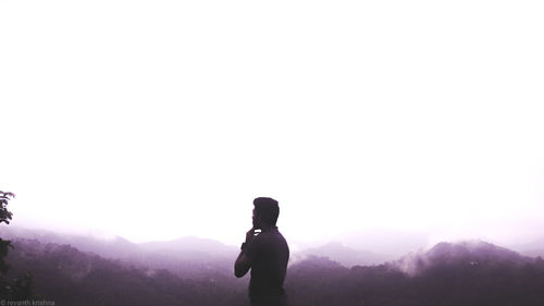 Rear view of man standing on mountain against clear sky