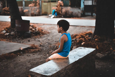 Side view of boy sitting on retaining wall