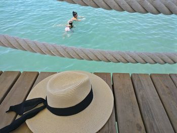 High angle view of hat on pier above woman with daughter swimming in sea