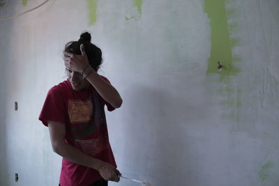 Man with head in hand standing against wall while painting at home