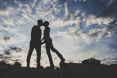 Low angle view of couple kissing against cloudy sky during sunset