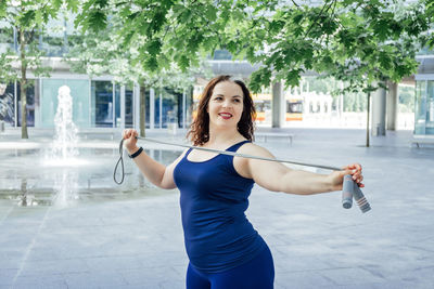 Confident plus size curvy happy young woman doing exercise workout with skipping rope outdoors.