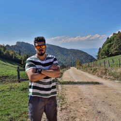 Portrait of confident young man wearing sunglasses standing on field during sunny day