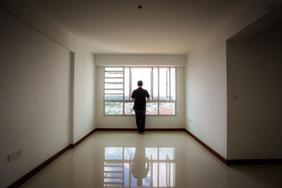 Rear view of man standing by window at home