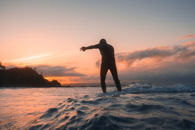 Rear view of man standing on beach against sky during sunset