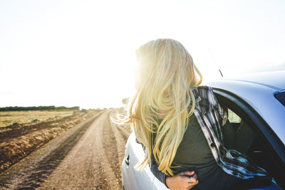 Young woman leaning out from car window against clear sky