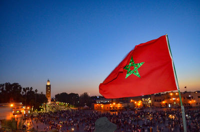 People at illuminated city against clear blue sky