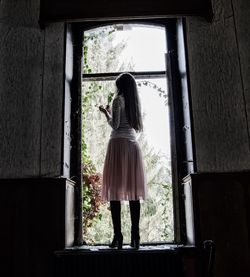 Full length rear view of woman standing on window sill