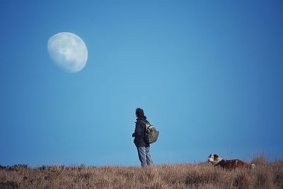 Man looking at moon while standing on field against clear blue sky