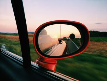 Close-up of side-view mirror against sunset sky
