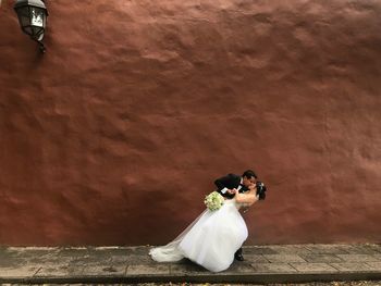 Bride and bridegroom kissing while standing against wall