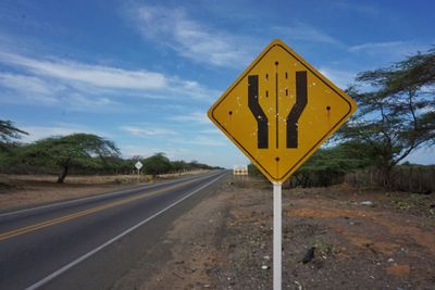 Road sign at roadside against sky