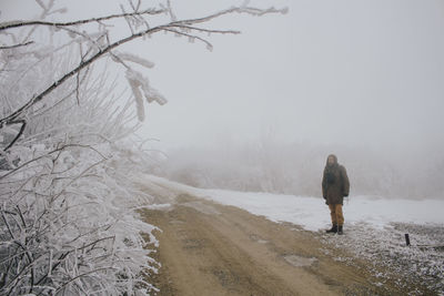 Man standing on snow covered field by empty dirt road during winter