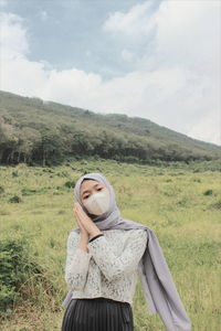 Portrait of young woman wearing mask standing on field