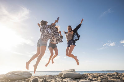 Friends jumping at beach against sky