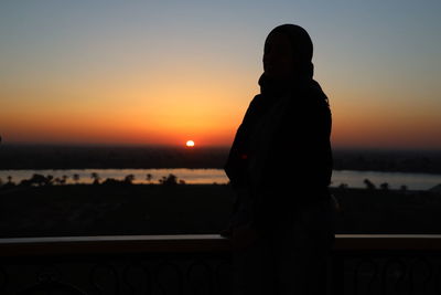 Silhouette woman standing by railing against sky during sunset