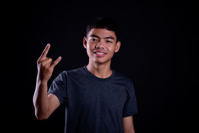 Portrait of teenage boy standing against black background