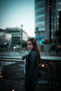 Portrait of woman standing against railing in city