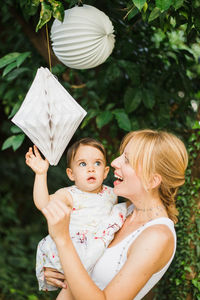 Mother carrying cute daughter touching decorations hanging in yard