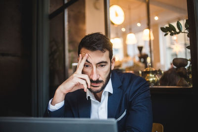 Tired businessman looking at laptop in creative office