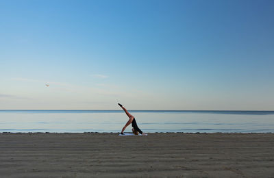 Yong women in pink leggins practicing yoga by the seaside against sky. 