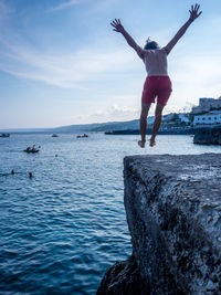 Rear view of man jumping in sea against sky