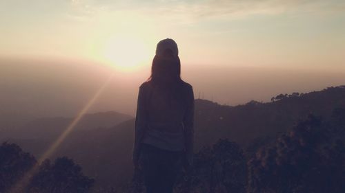 Rear view of silhouette woman standing on landscape at sunset