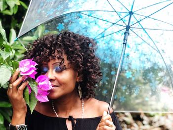 Mature woman with curly hair holding umbrella while smelling flowers