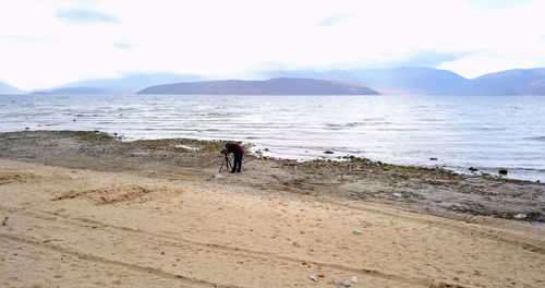 Man with tripod standing against sea at beach