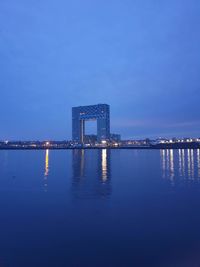 Illuminated buildings by sea against sky at dusk