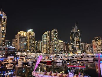 Boats moored at harbor against buildings in city at night