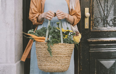 Woman holding wicker shopping bag by door
